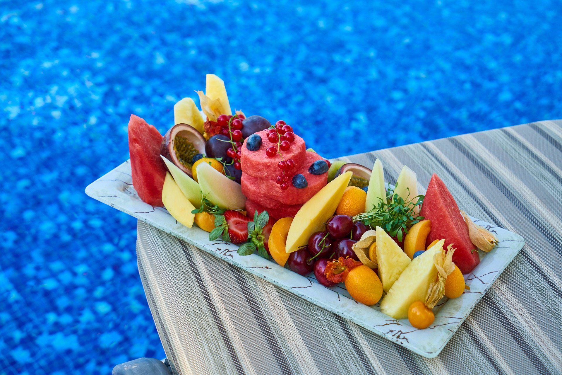 platter of cut fruit varieties on pool deck overlooking blue pool water