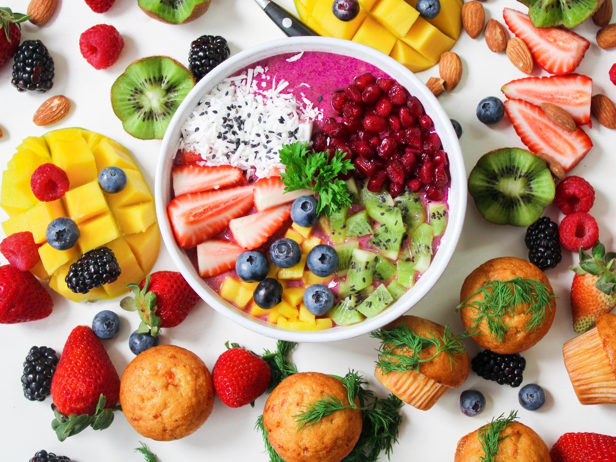 an assortment of fresh fruits mango, strawberries, blueberries, raspberries, kiwi, muffins